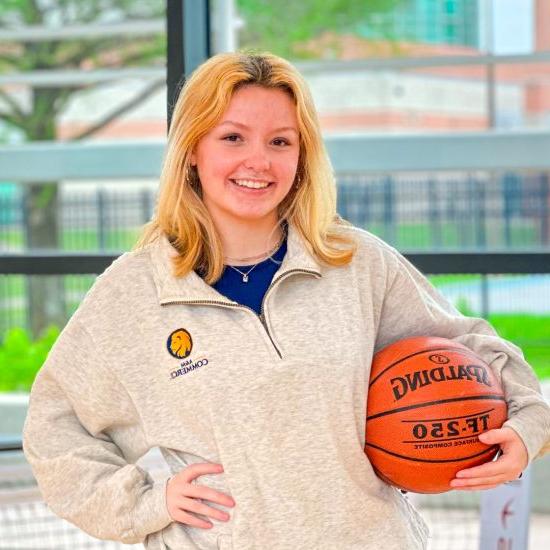 A young woman poses holding a basketball on her hip.